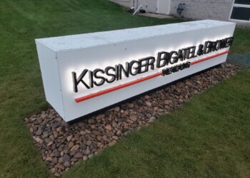 Illuminated sign on a stone base reads "Kissinger Bigatel & Brower REALTORS," located on a grassy area.
